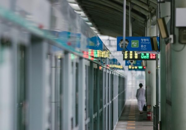 地铁车厢里一位乘客低头看手机，屏幕上是问鼎h5在线的浅色页面，车厢灯光偏冷形成对比